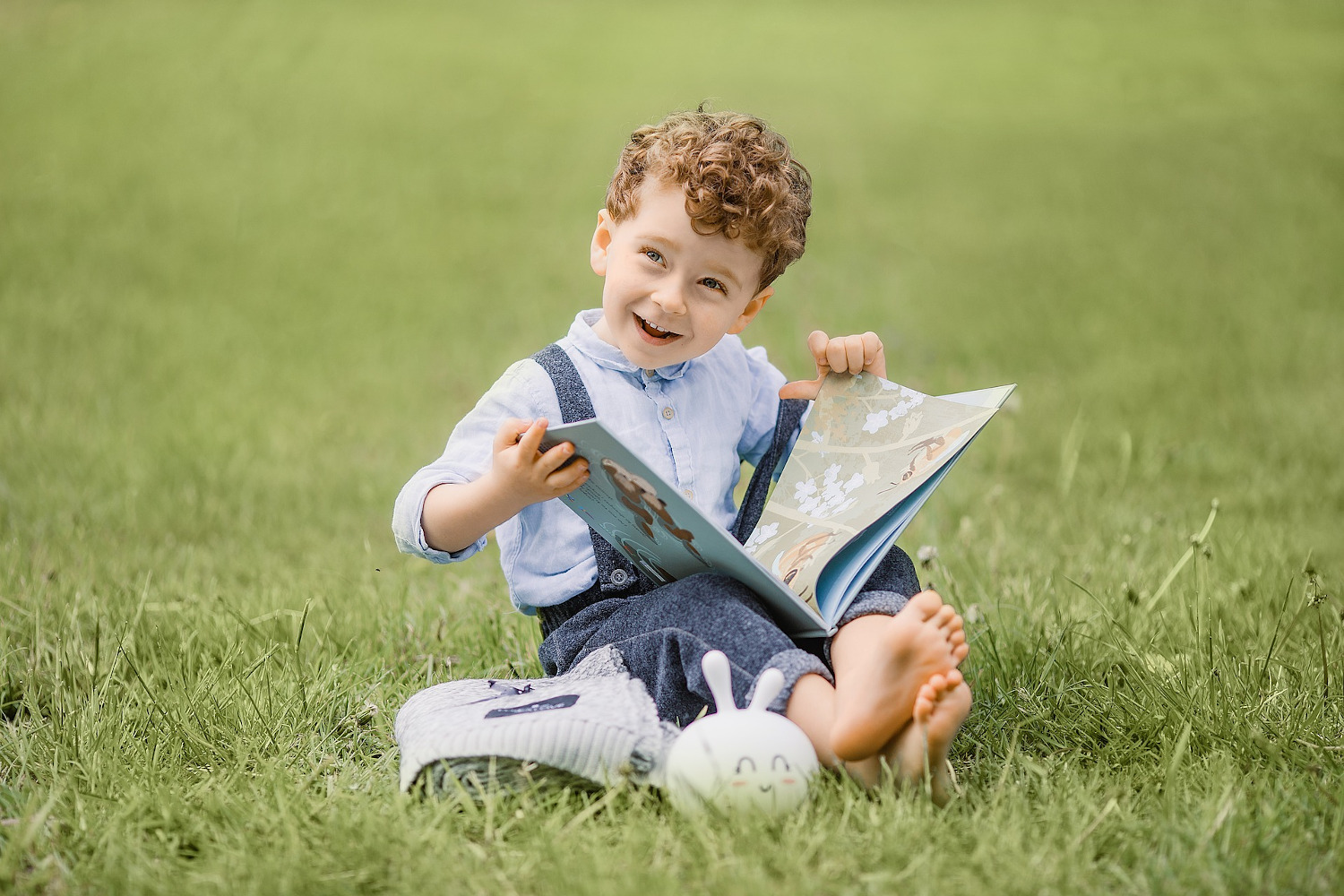 Ein kleiner Junge sitzt mit einem Buch auf einer grünen Wiese und freut sich